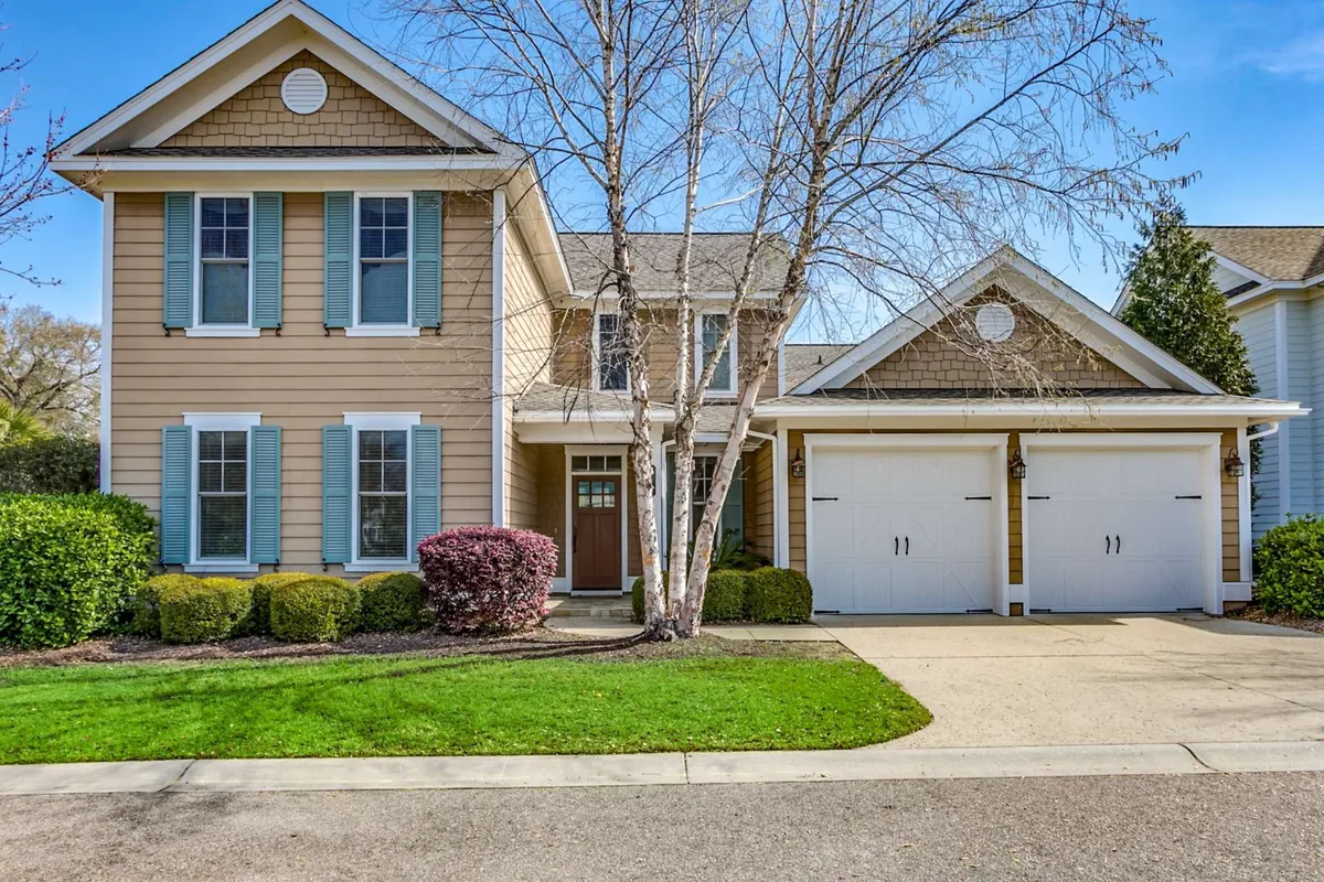 A welcoming exterior shot of the home's front entrance, featuring garage doors, a landscaped yard with mature trees, and a sunny porch. The scene evokes a sense of comfort and togetherness, ideal for group retreats.