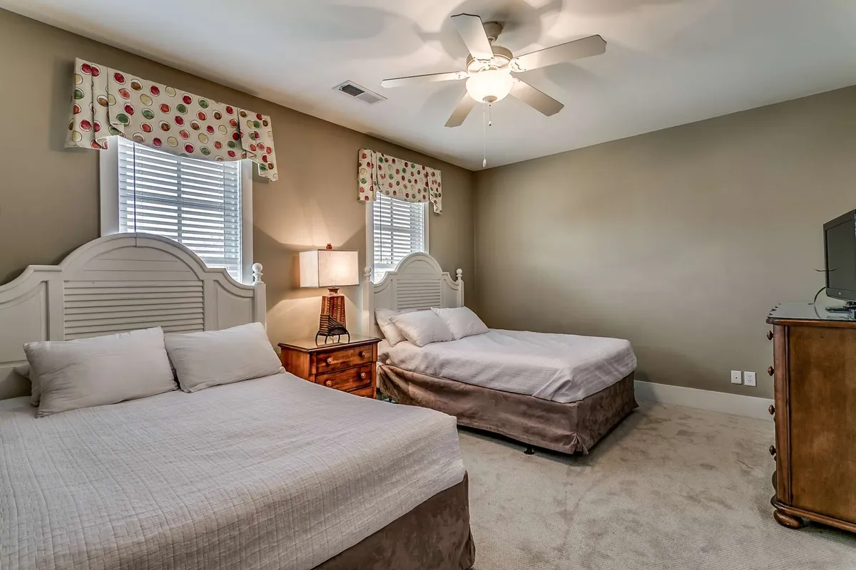 A comfortable guest bedroom with two beds, nightstand and lamp, a small dresser, and window treatments creating a cozy ambiance. The setup suggests flexibility for families or friends sharing a space, with personal touches and a sense of warmth.