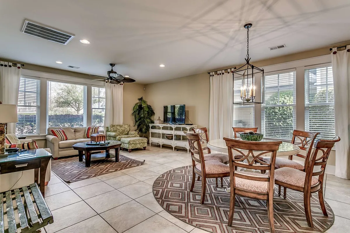 A view of the open-concept living and dining area, highlighting a central dining table, sofa set, television unit, and patterned flooring. Large windows let in abundant natural light, and the layout seamlessly connects lounging and dining spaces, promoting easy social interaction.