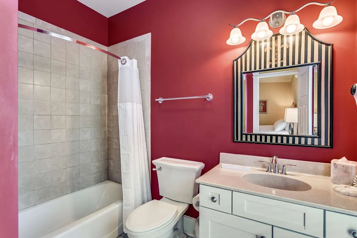 A modern, vibrant spa-inspired bathroom with a red accent wall, framed mirror, and elegant bath fixtures. The space is inviting for self-care, grooming, and unwinding after a day at the pool or fitness center.