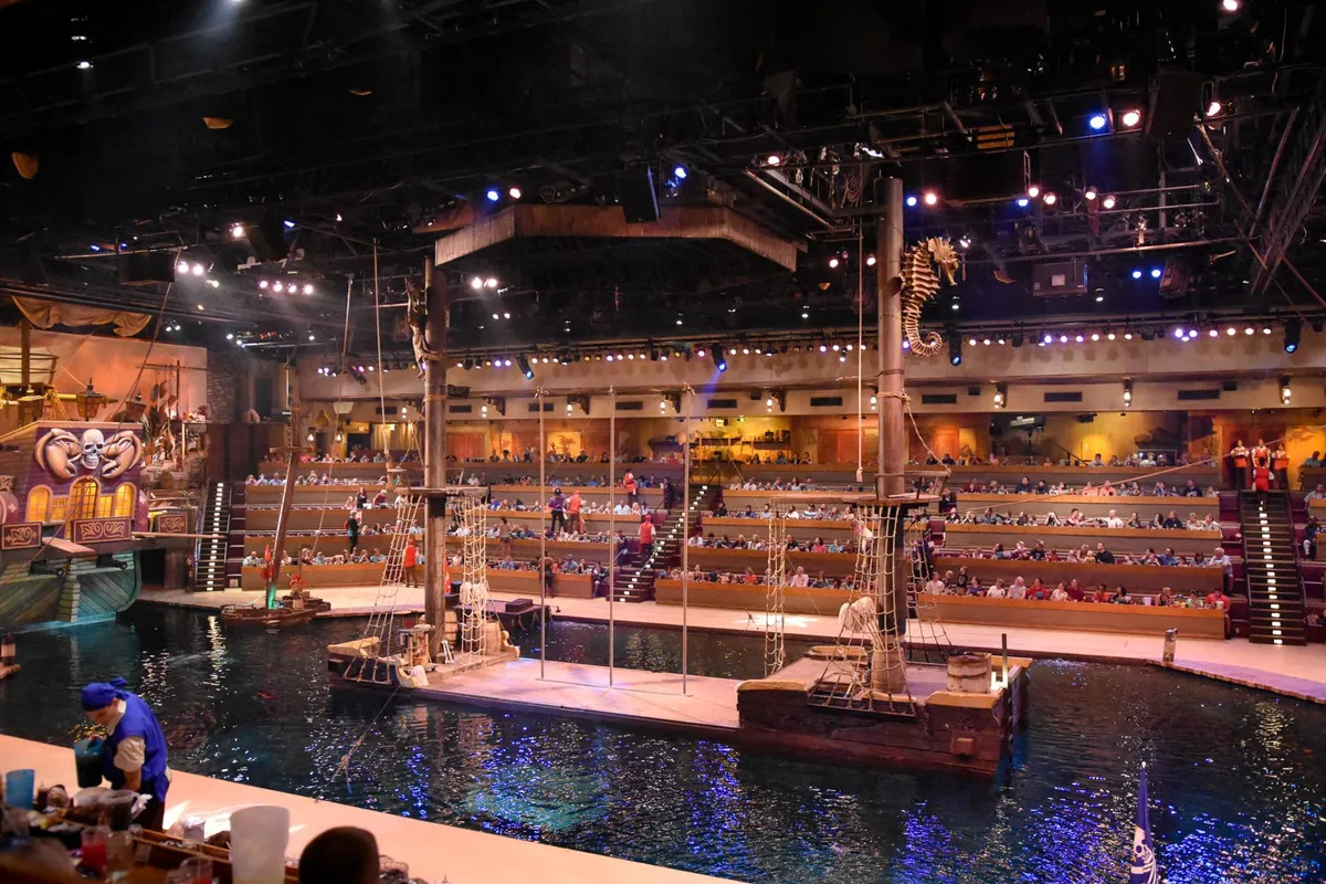 A dynamic interior performance setting featuring a staged pirate ship, vibrant performers, and a captivated audience. Water effects and immersive lighting create an energetic, theatrical mood perfect for special evenings out.