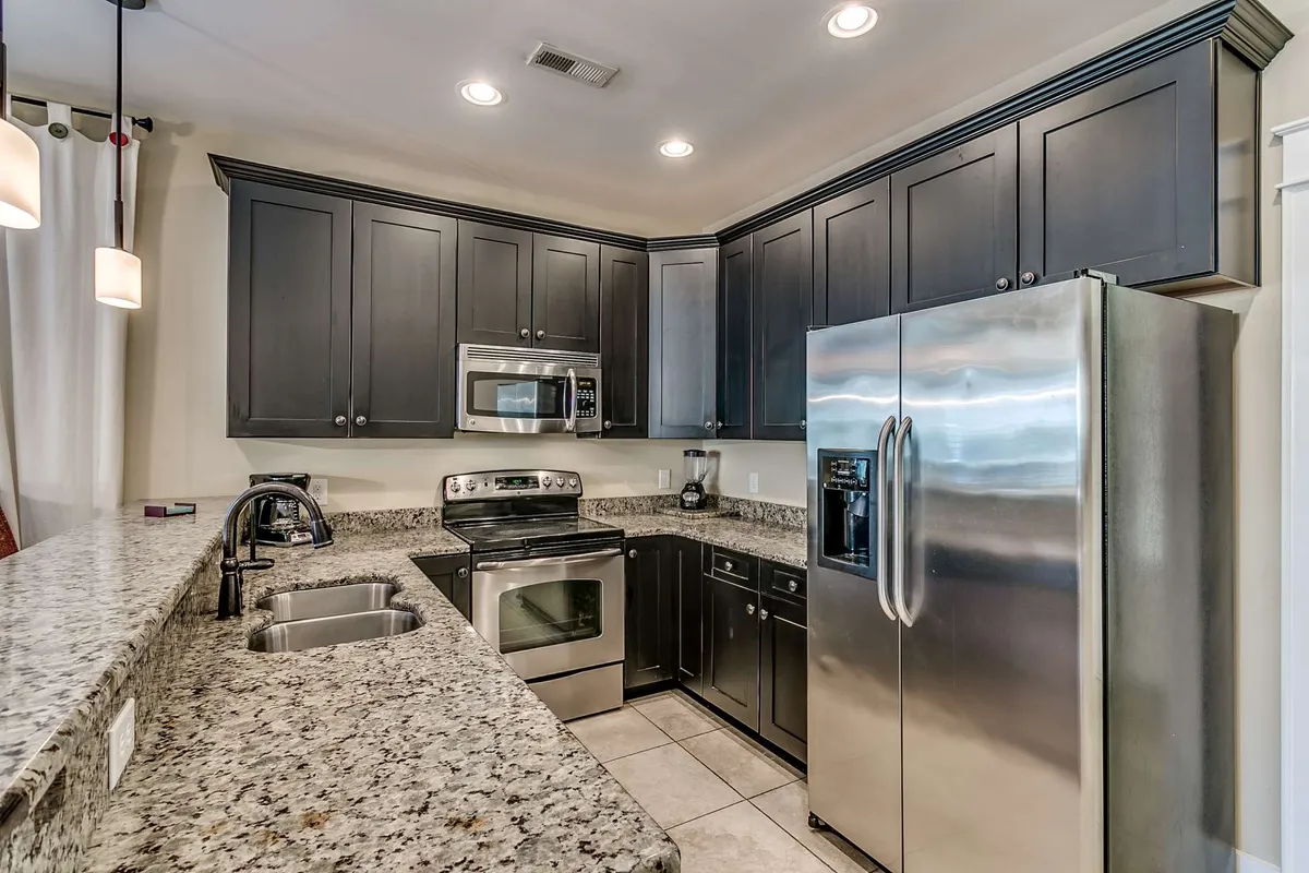 A view of the kitchen showcasing a spacious granite countertop, sleek stainless steel appliances, and rich dark cabinetry. The image radiates a modern, inviting feel and gives a clear indication of a fully equipped, contemporary cooking space.