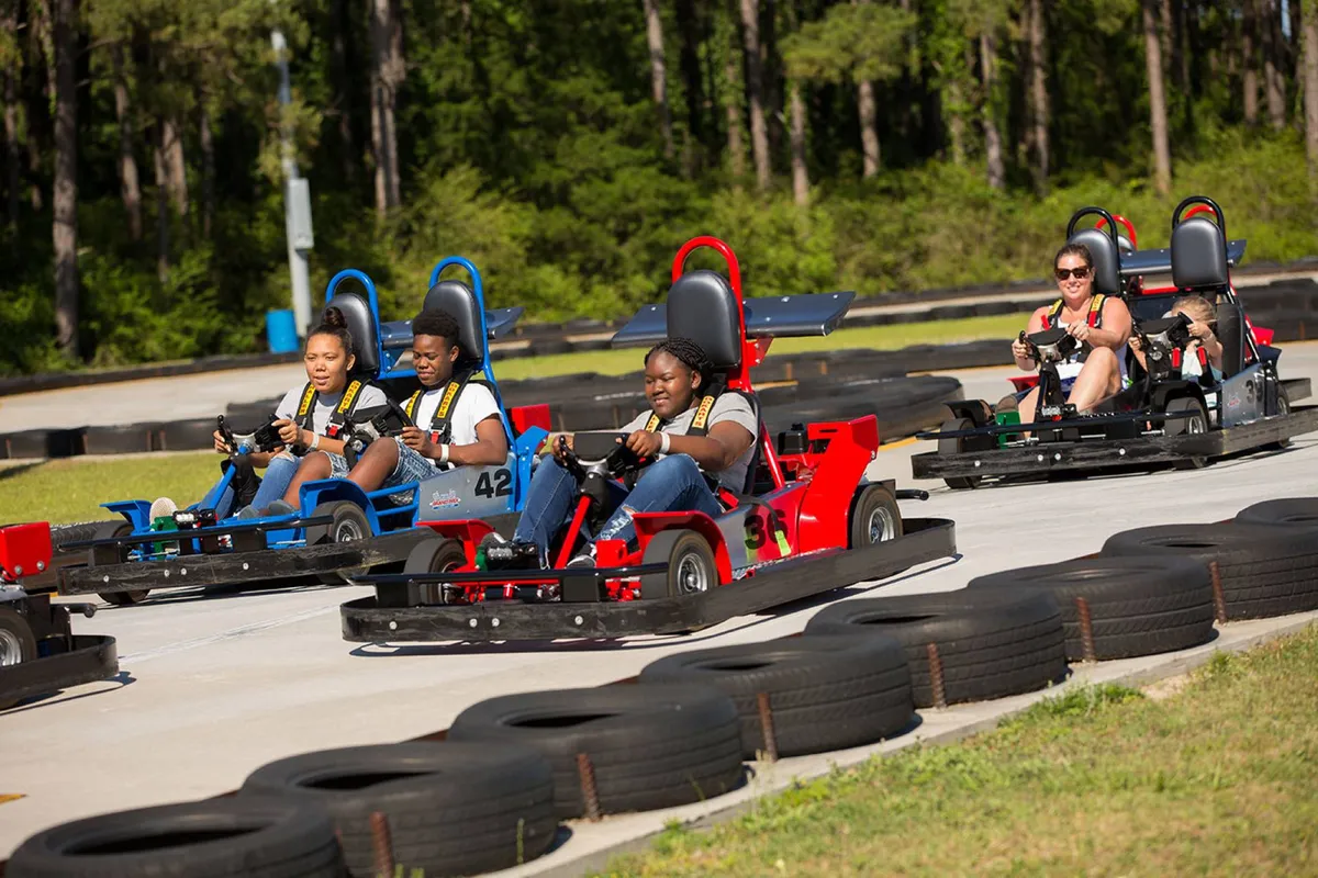An action-packed exterior shot of a racetrack with go-karts in motion and families enjoying friendly competition. The lively scene is filled with excitement and highlights the thrill of local attractions available to guests.